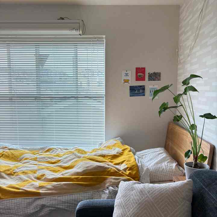 北欧風のナチュラルな寝室で、木製ベッドに黄色いブランケット、観葉植物とポストカードが雰囲気良く配置された印象的な空間