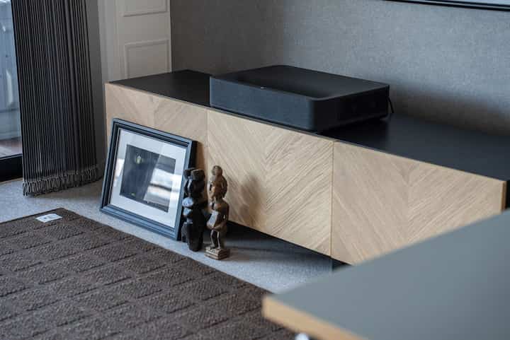 Living room with a beige wooden TV stand featuring a black projector on its black surface and a brown carpeted floor