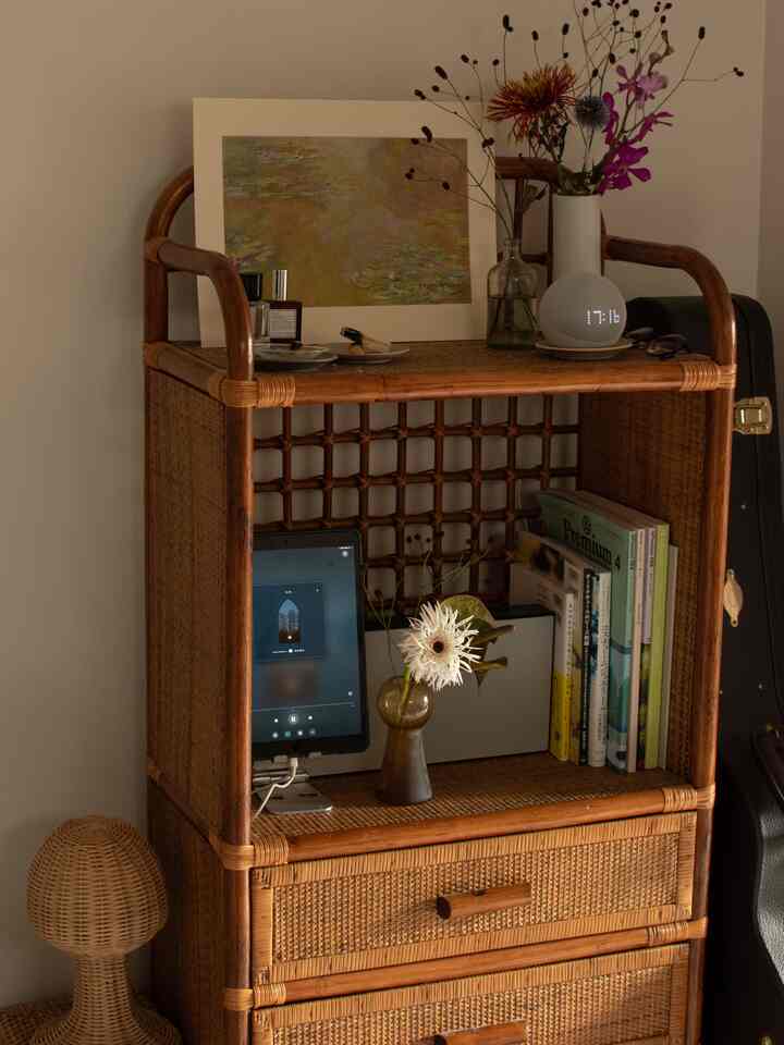 Warm orange-brown toned studio apartment featuring a 30-year-old vintage rattan cabinet centrally with decorative flowers and electronic devices, creating cozy atmosphere