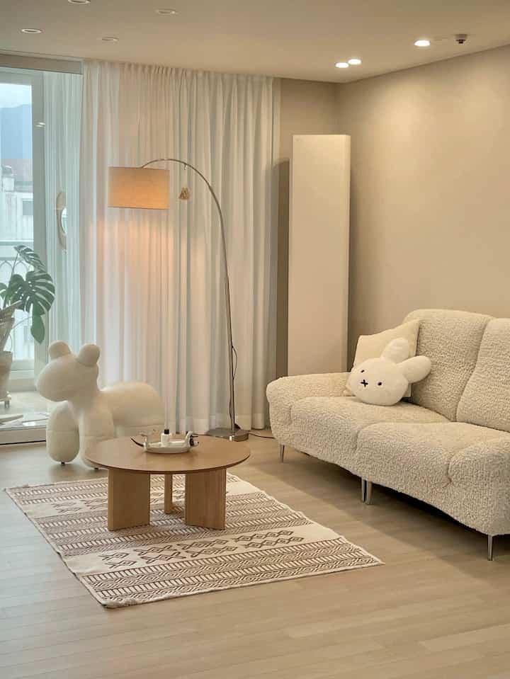 ナチュラルカラーとホワイトのトーンのリビング、ベージュのソファと円形のコーヒーテーブルが配置されたシンプルで落ち着いたインテリア