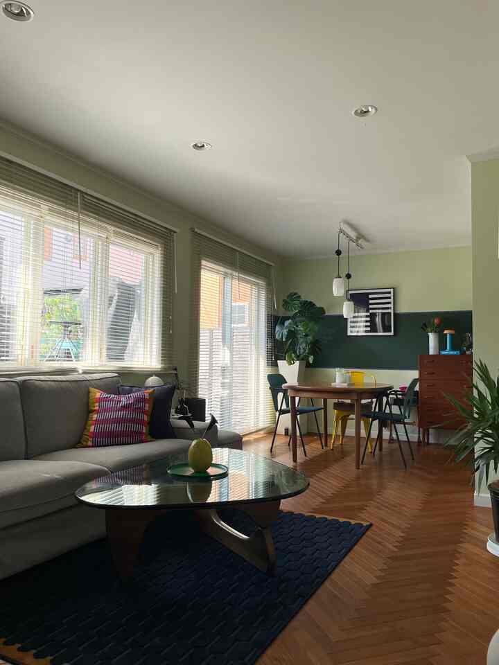 Natural-toned living and dining room featuring a gray sofa and wood-tone dining table with bright windows.