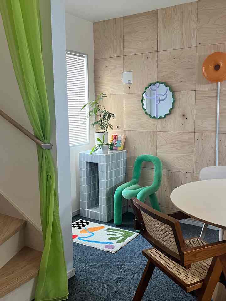 Green-toned dining room featuring a wood panel wall, colorful carpet, unique chairs, and a decorative mirror