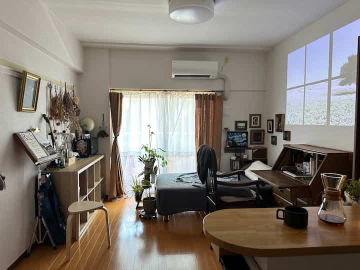 白と茶色の色調の一人暮らしワンルーム、自然光と机、ベッドが調和した温かみのある空間