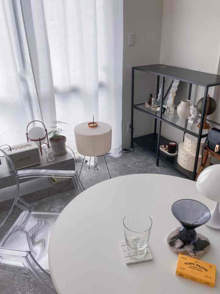 モノトーンの一人暮らしリビング、透明な椅子と円形テーブル、アカリのフロアランプが配置されたシンプルな空間