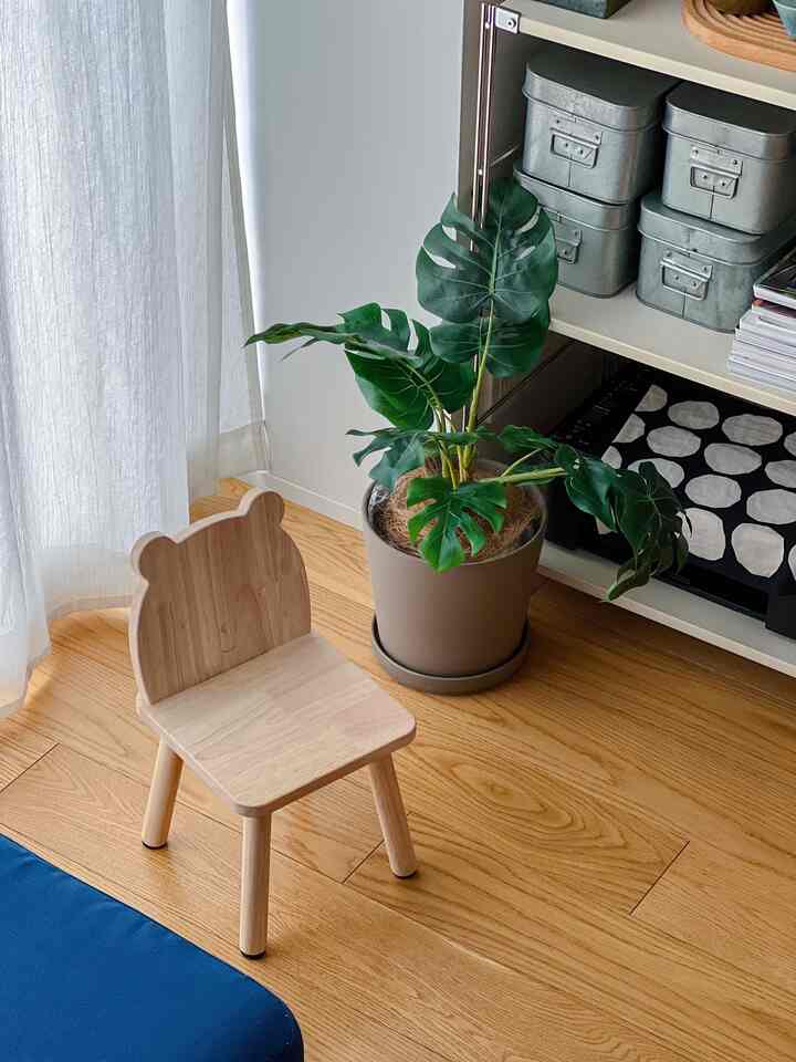 明るい木目調の床と自然光が差し込む子供部屋、クマの顔が形どられた木製のキッズチェアと鉢植えが配置された温かみのある空間