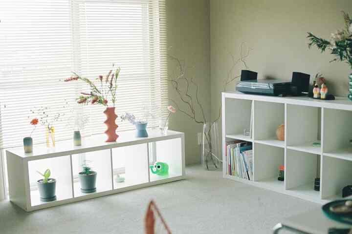 白とベージュのトーンのリビング、白いKALLAX棚に花瓶と植物が配置されたすっきりしたインテリア