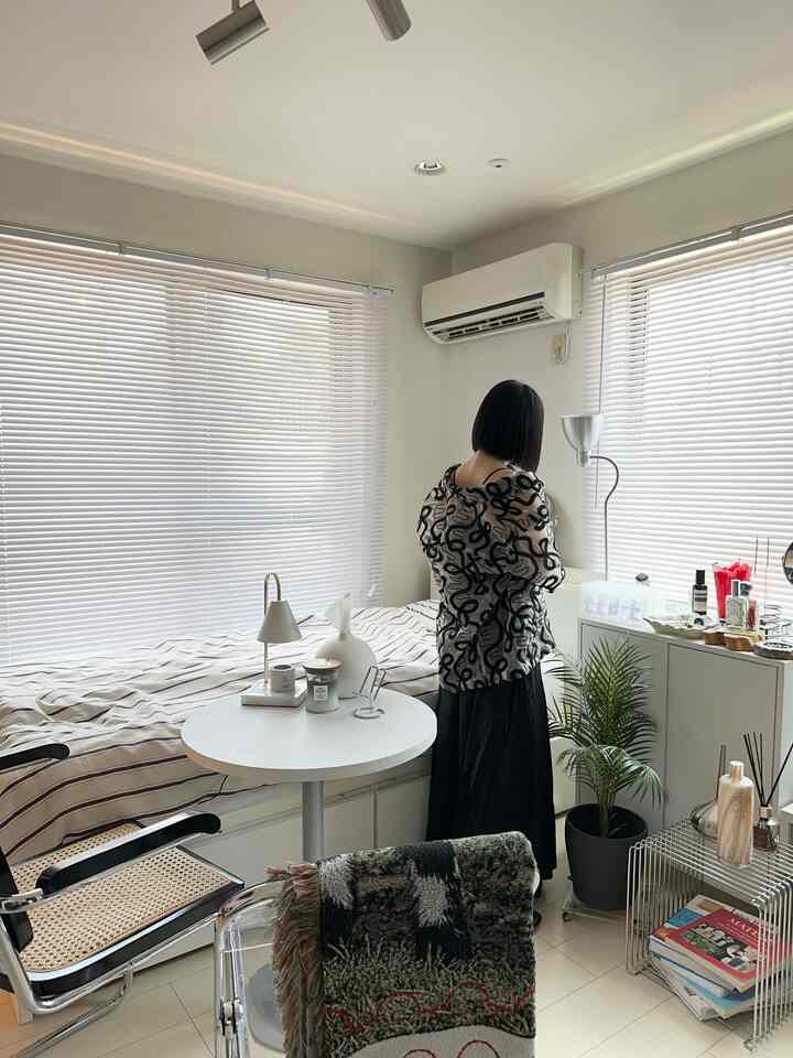 白とナチュラルな色合いの8畳1Kの部屋、丸いダイニングテーブルとラタンチェア、収納キャビネット、観葉植物が配置された温かみのある空間