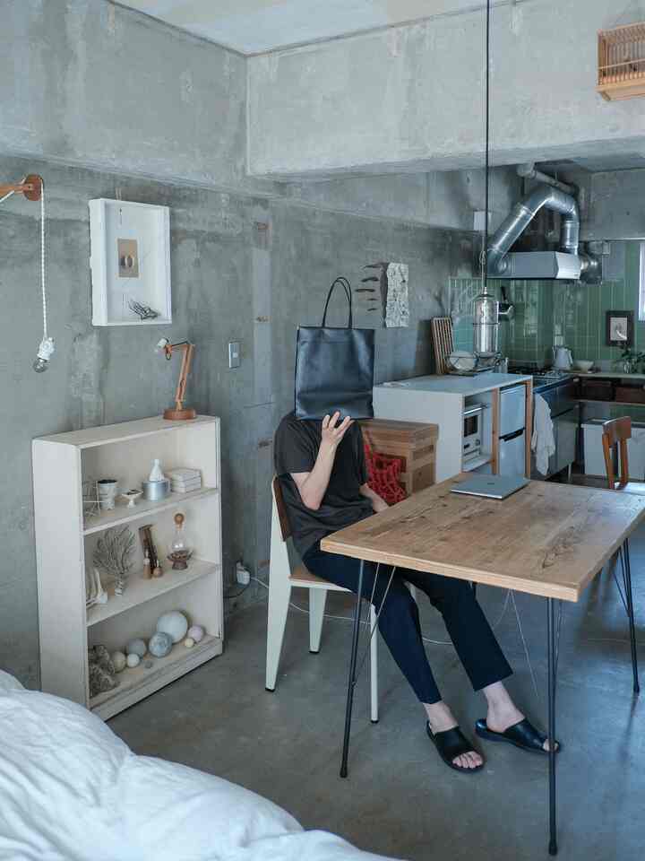 グレーのコンクリート壁と木目調のテーブルが配置された一人暮らし向けのナチュラルモダンなリビングとキッチンの雰囲気のあるインテリア