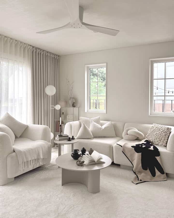 Warm white and beige toned living room featuring curved sofas, a coffee table, and a black bear accent throw