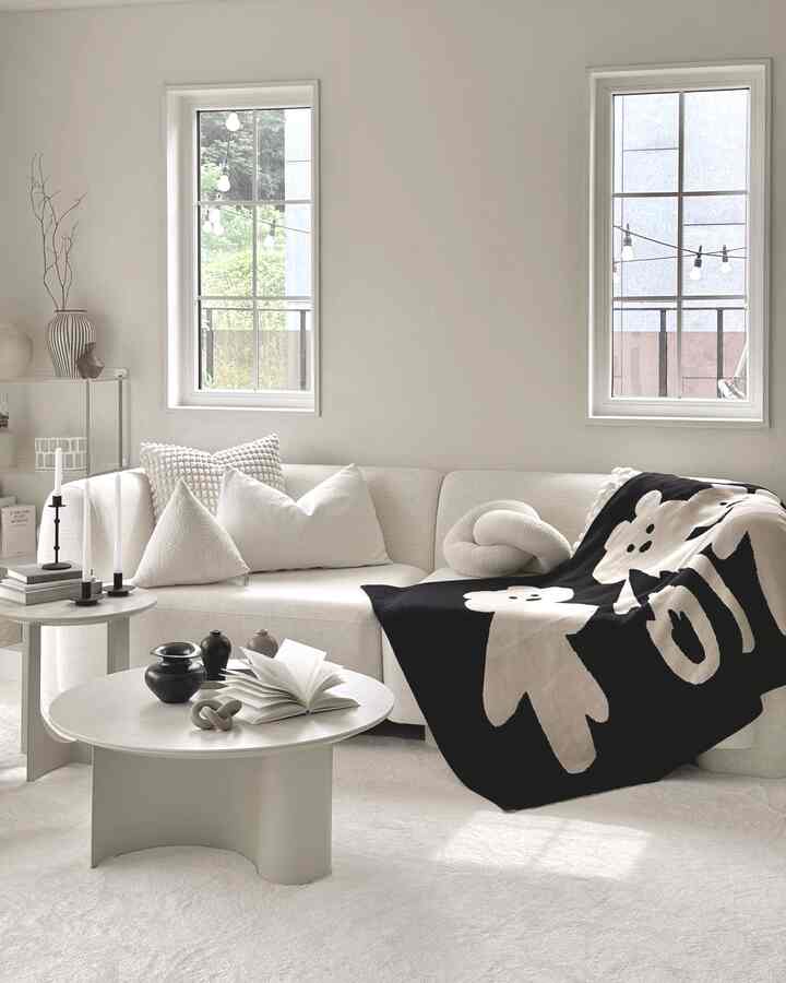 ホワイトとブラックのトーンのリビング、コーナーソファとラウンドコーヒーテーブル、パターン付きスローが配置された落ち着いた空間