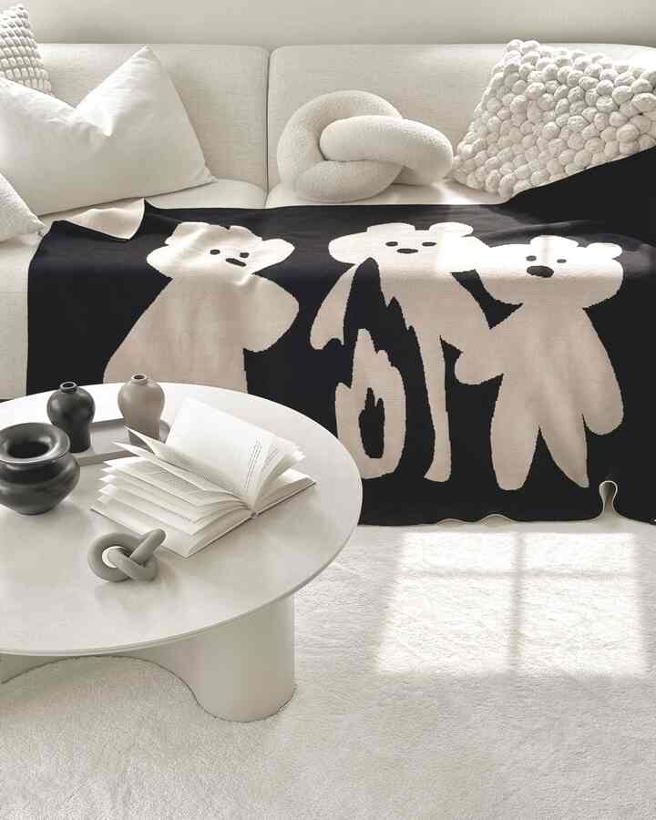 Natural tones living room featuring beige sofa with black bear throw, white rug, and coffee table creating a cozy atmosphere