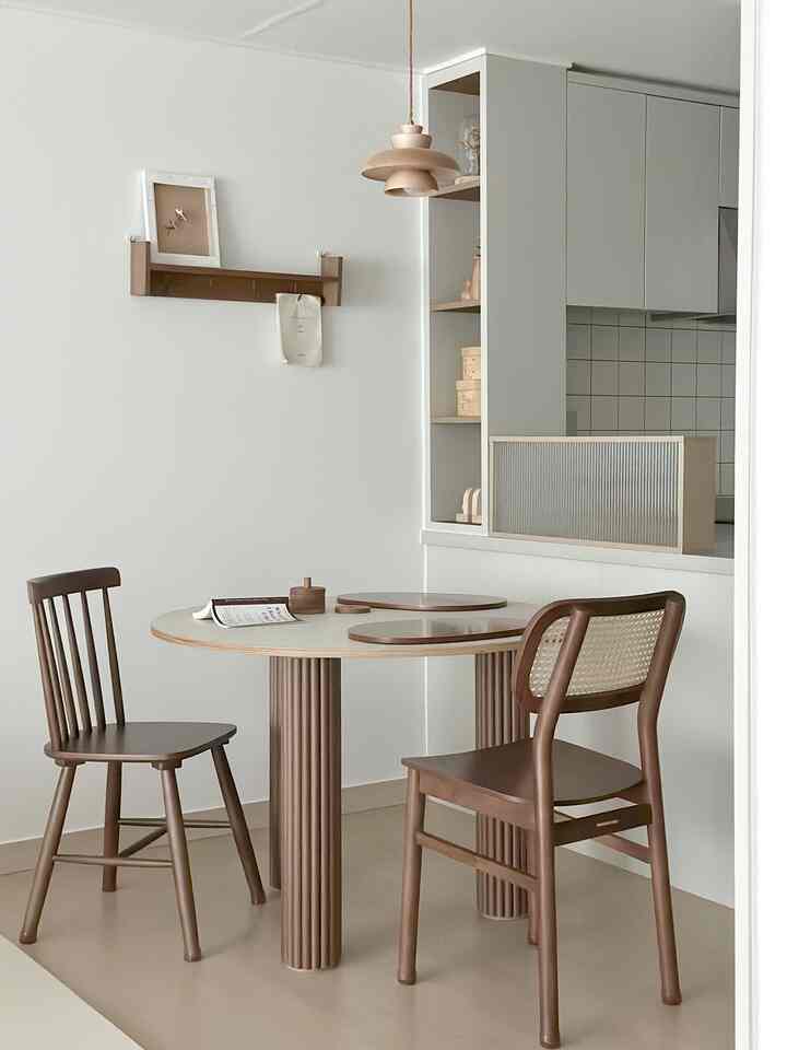 Natural color and white toned dining room featuring a round dining table, wooden chairs, and a pendant light with a simple atmosphere