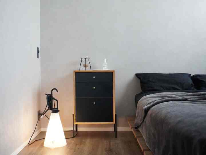 白い壁とナチュラルな木目調の床、黒い寝具とチェストが配置されたモダンでミニマルな寝室の雰囲気のあるインテリア