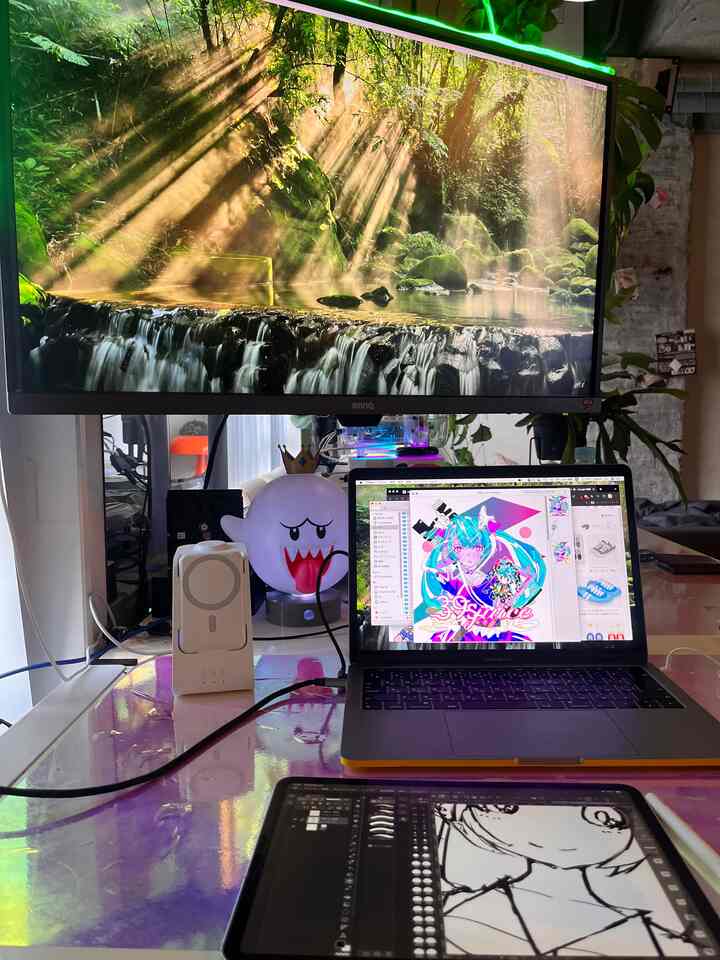 緑の植物が背景にある、黒いモニターとタブレットが置かれたワンルームのワークスペース