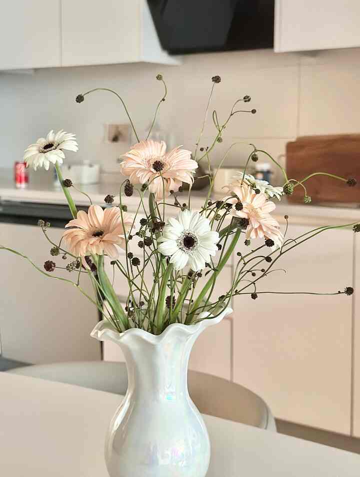 Kitchen space in white and beige tones featuring an iridescent ceramic vase with soft flowers, creating a minimalistic atmosphere