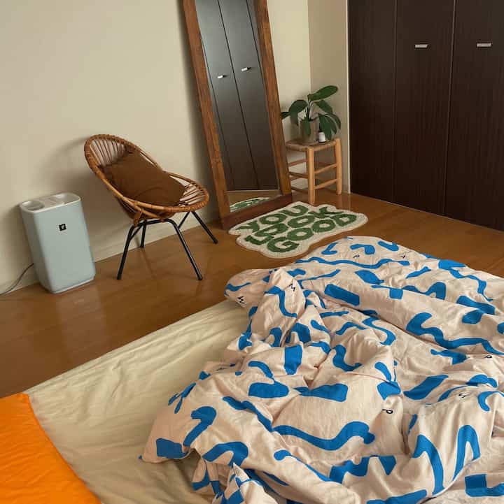 白と木目調の寝室、ベッドとラタンチェア、大きな全身鏡が配置された落ち着いた雰囲気のインテリア