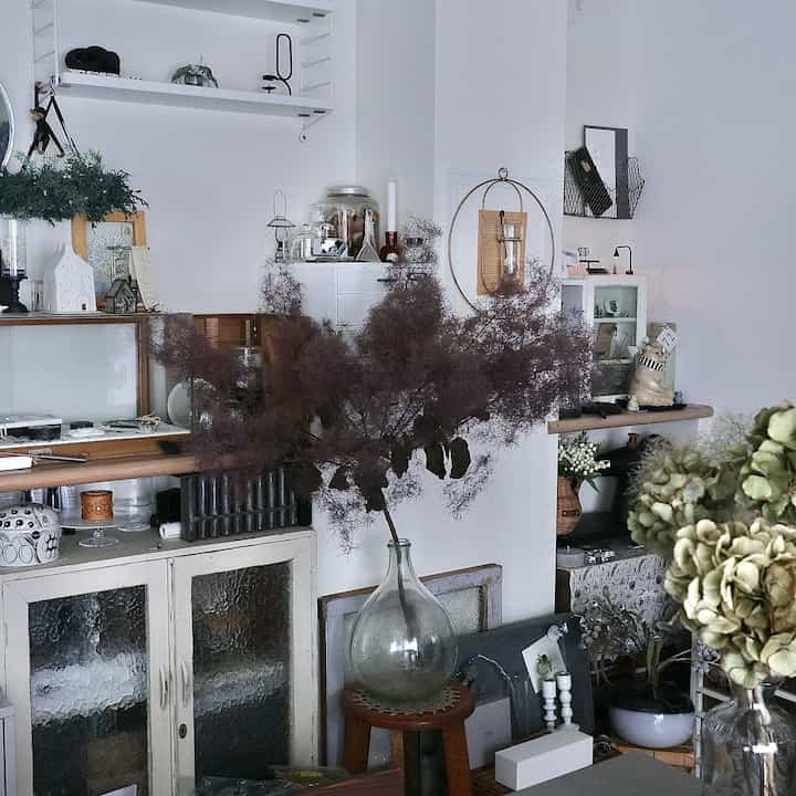 白い壁とヴィンテージ家具が配置されたナチュラルな色調のダイニング、中央に大きなドライフラワーが印象的な空間