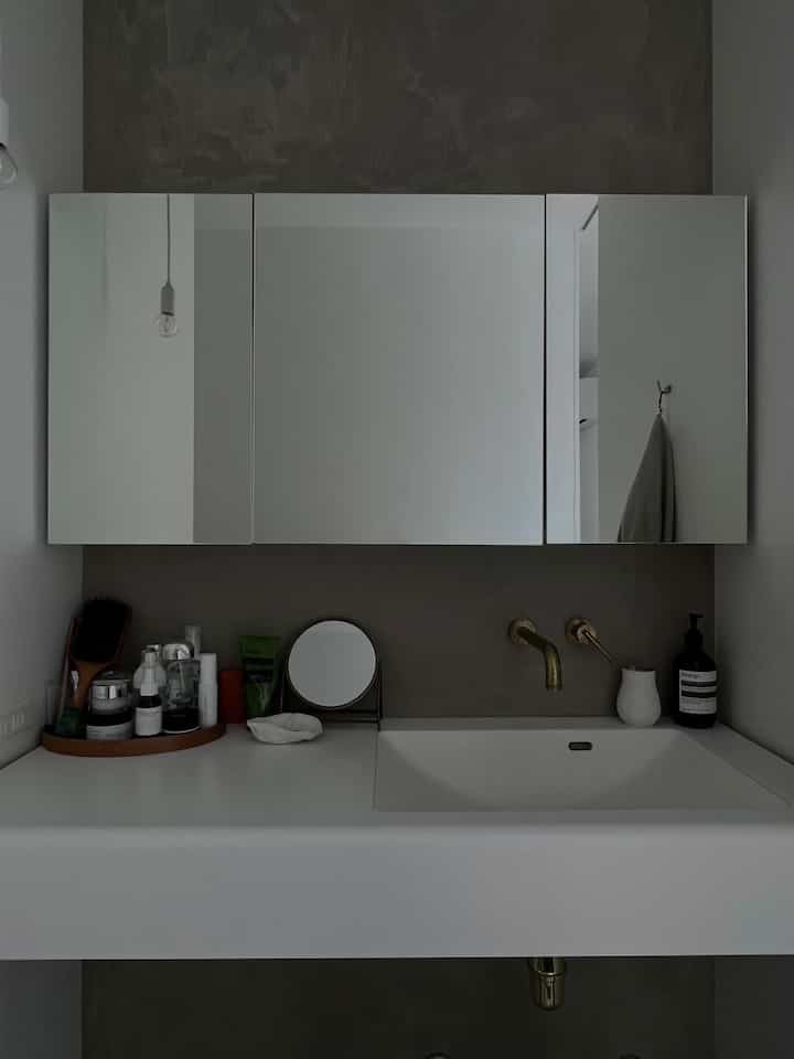 グレーのトーンが印象的なパウダールーム、ゴールドの水栓と大きな鏡キャビネットが配置されたシンプルな空間