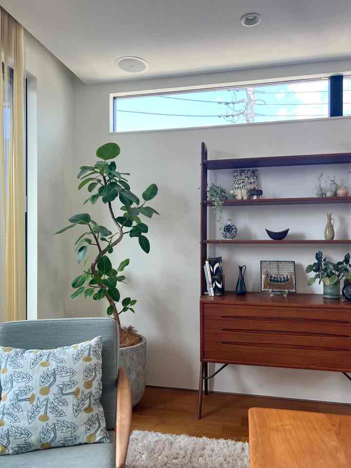 Bright white-walled Scandinavian living room featuring wood-toned furniture and green plants with a simple, cozy atmosphere