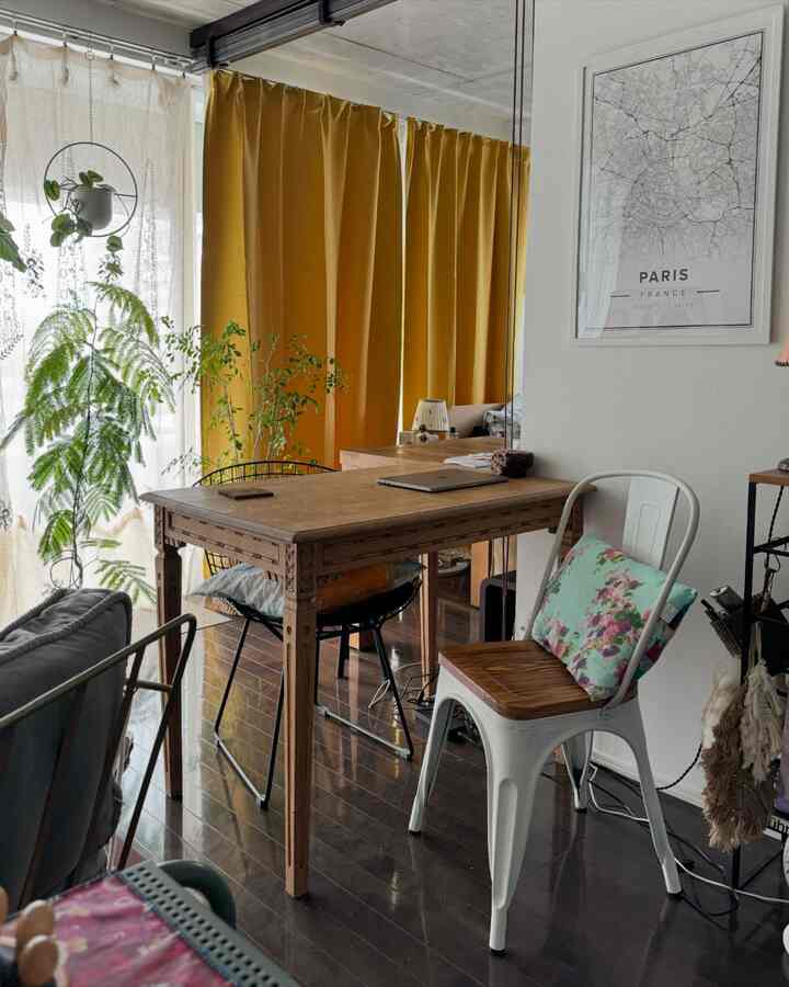 マスタードイエローのカーテンと無垢材のテーブルが置かれたリビング、緑の植物と白いダイニングチェアが調和する自然な雰囲気のインテリア