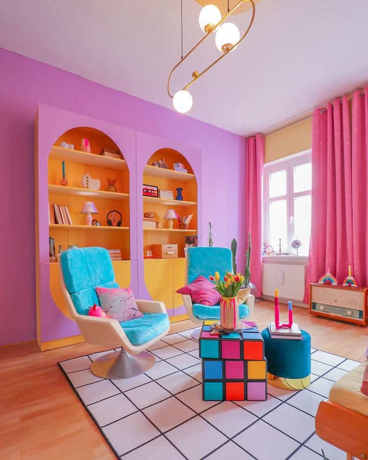 Vibrant living room with purple walls, yellow shelving, blue armchairs, and pink curtains creating colorful ambiance