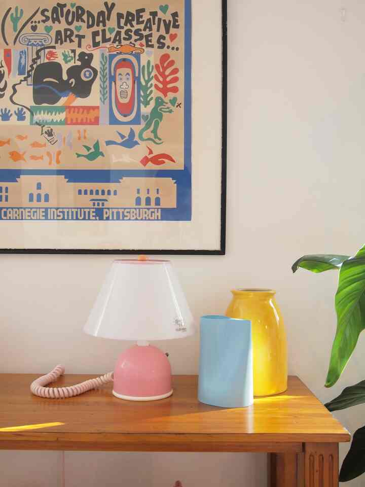 暖かみのある木目調のテーブルに、ピンクのランプと黄色・青の花瓶が置かれたレトロなリビング空間