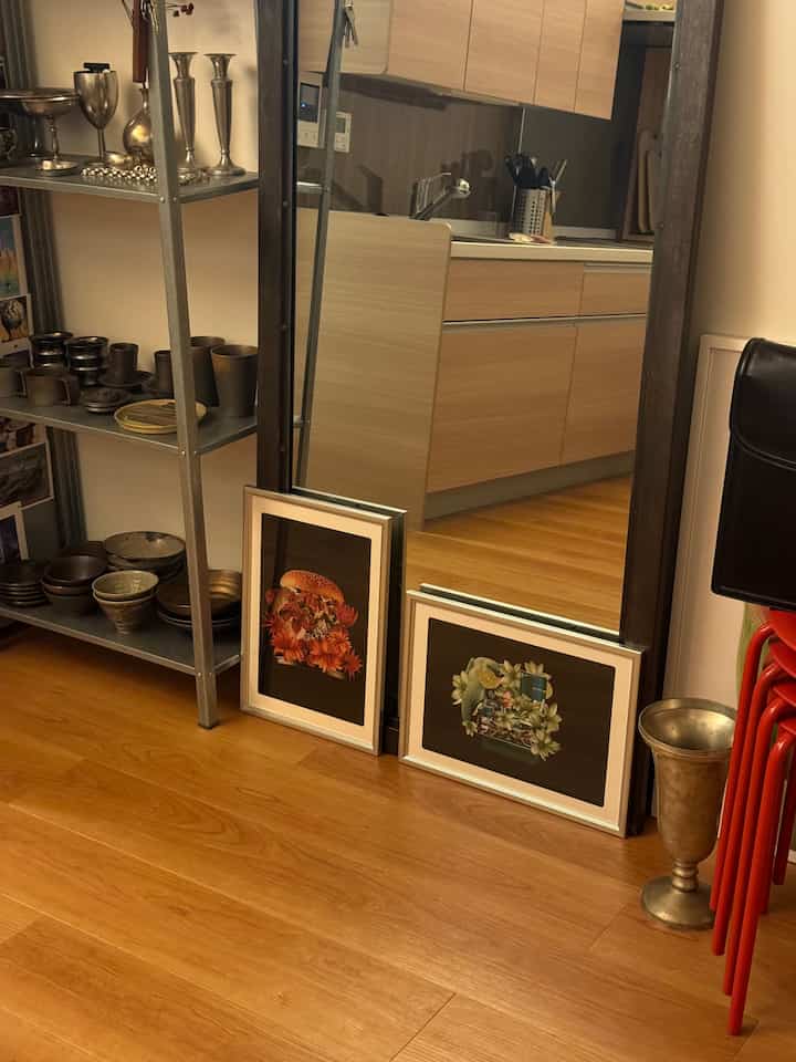 Warm wood-tone small kitchen space with metal shelving, framed pictures on floor and stacked red stools, creating a modern interior