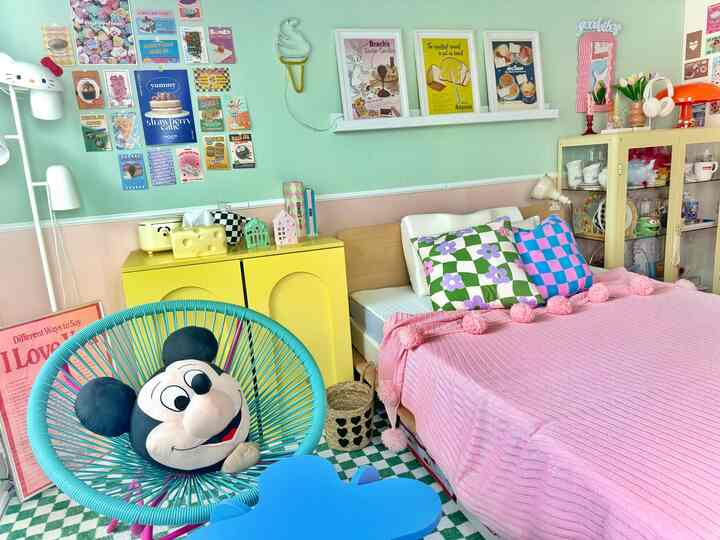 ミント色の壁と黄色のキャビネットが配置された一人暮らしの寝室、ピンクの寝具とカラフルなポスターが印象的な空間