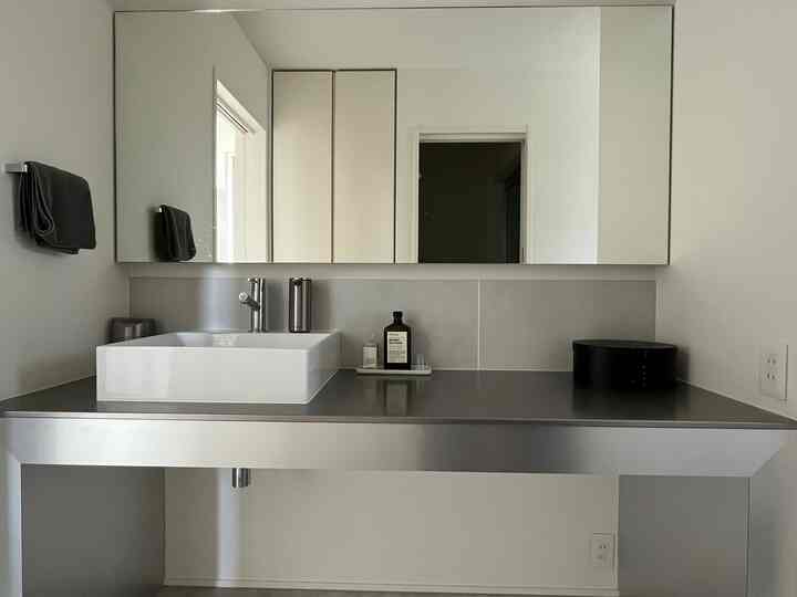 白とステンレスのシンプルな洗面台が配置されたモダンなバスルームのインテリア