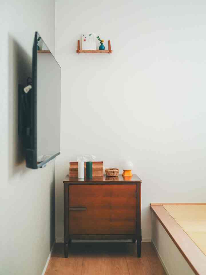 White-walled bedroom corner featuring a wood-tone vintage nightstand and tatami platform in a Mid-Century Modern style