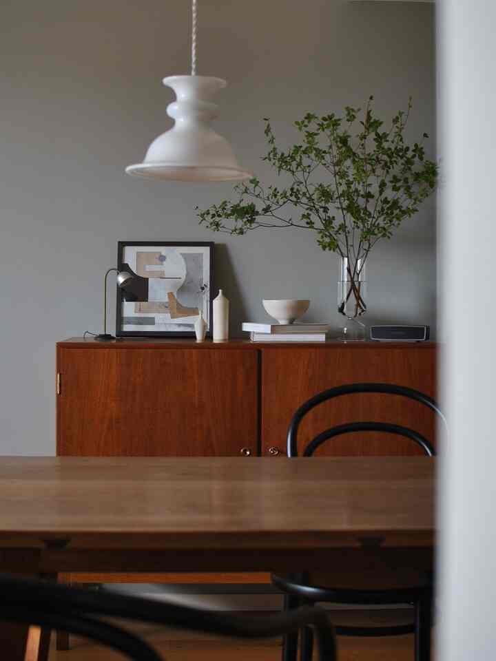 グレーの壁にウッドトーンのダイニングルーム、透明な花瓶と額縁が配置されたシンプルなインテリア