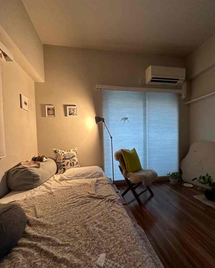 A beige and light brown toned single household living room featuring a simple bed, floor lamp, and cozy natural atmosphere