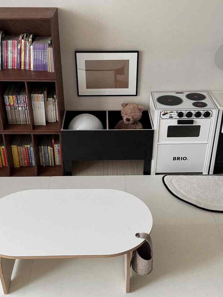 白と茶色の色調の子供部屋、玩具キッチンや収納箱、本棚が配置された温かみのある自然な雰囲気のインテリア