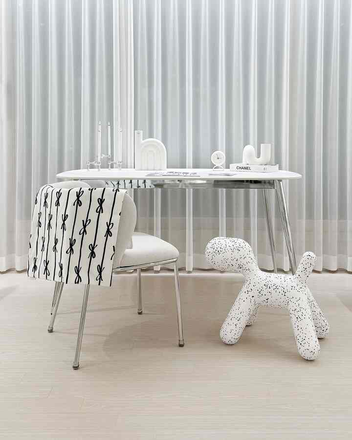 白とベージュのトーンの空間、中央にデスクと椅子が配置され、ペットを連想させる独特なデザインのスツールがあるミニマルなインテリア