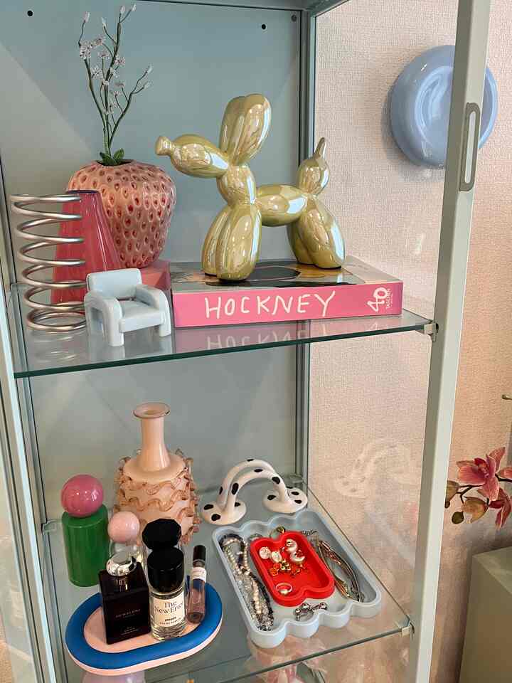 白とピンクのトーンのリビング、ガラスのキャビネットに花瓶や様々な装飾品が配置された雰囲気のあるインテリア