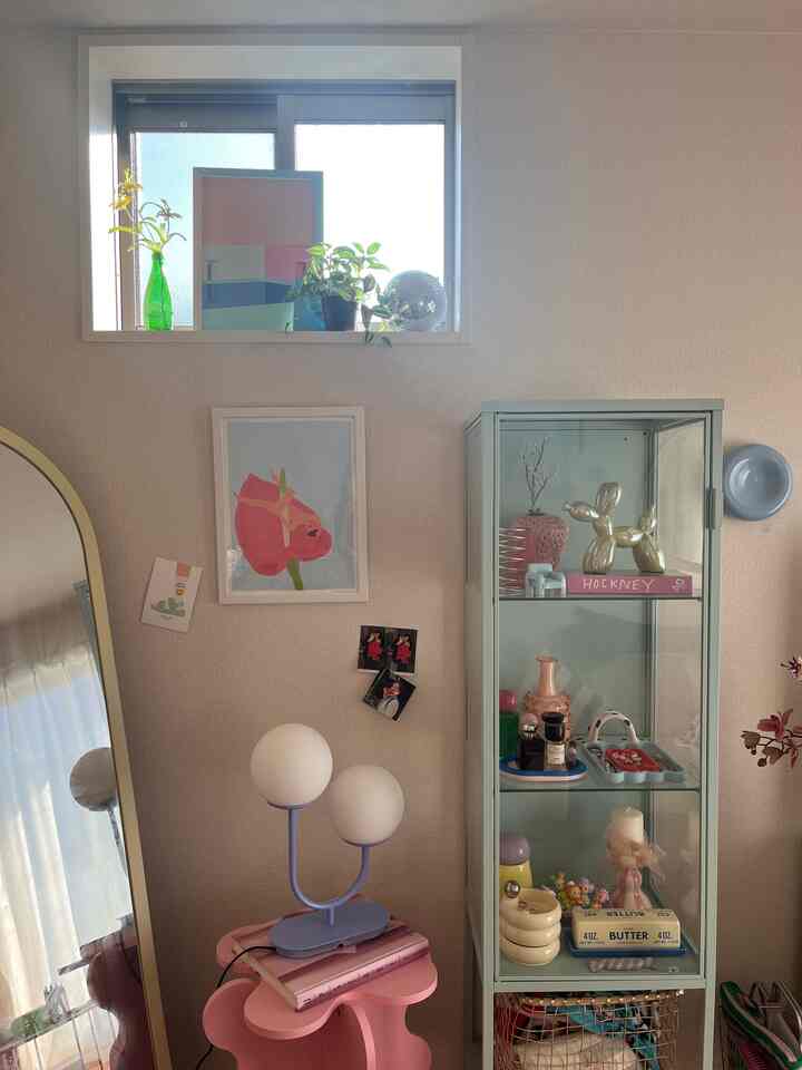 ナチュラルカラーの壁とピンクのサイドテーブル、ガラス製の飾り棚が配置された居心地の良いリビングインテリア