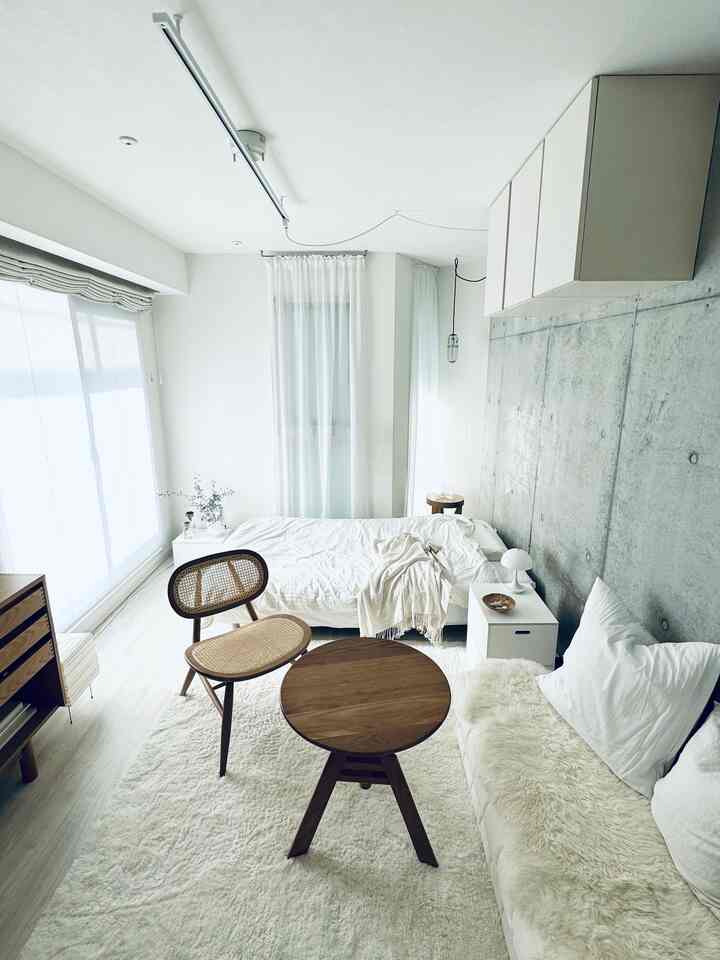 White and wood tone studio bedroom featuring minimal natural furniture with a cozy, simple atmosphere