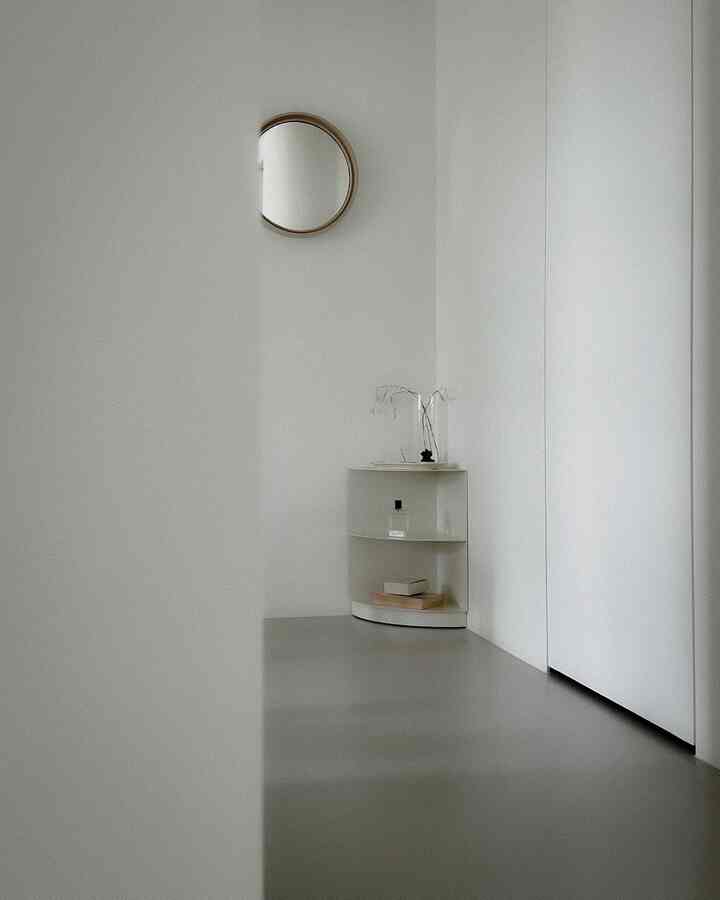 ホワイトトーンのすっきりとしたコーナースペース、パイピーのクォーターシェルフと木製の丸い鏡が配置されたモダンなインテリア