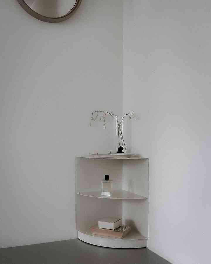 白い壁とコーナー棚が配置されたミニマルな空間、少数の本やオブジェが置かれた雰囲気のあるインテリア