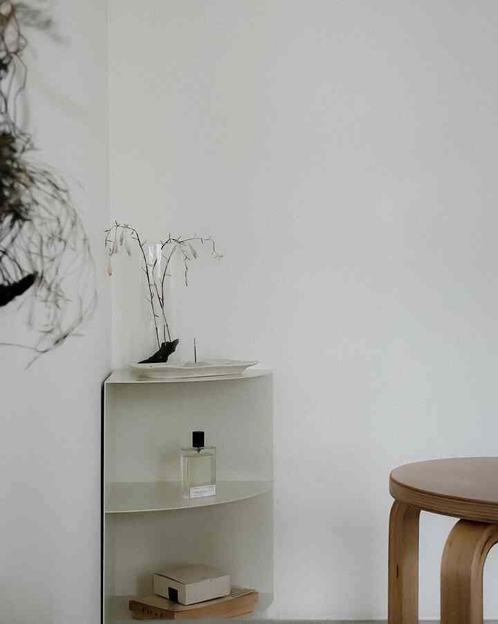 白とナチュラルカラーのリビング空間、コーナー棚と木製スツールが配置されたミニマルなインテリア