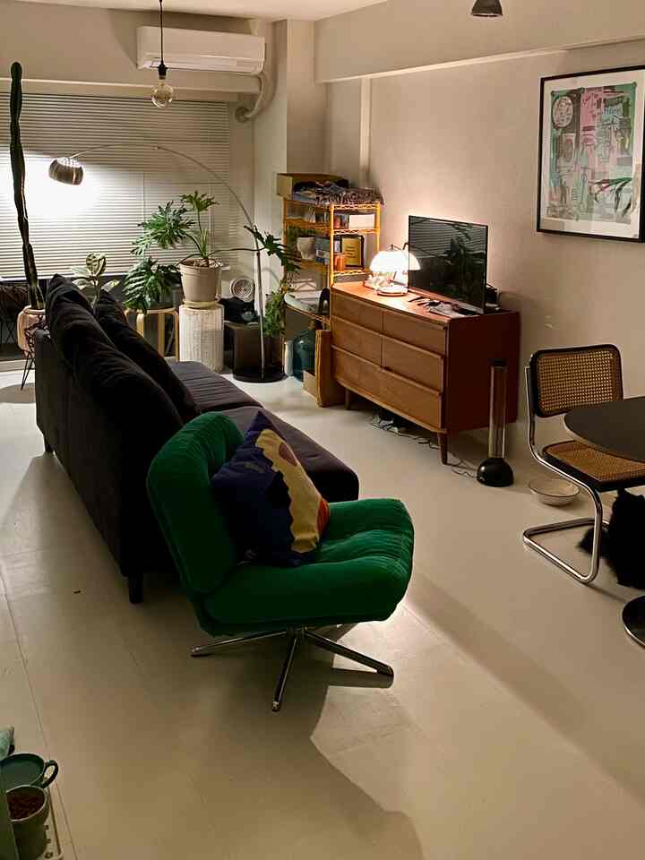 ナチュラルカラーと黒を基調としたリビング、緑のアームチェアとソファ、バスキアのポスター、複数の植物が配置された雰囲気のある空間