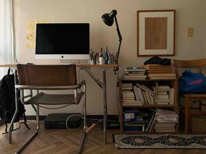 Subtle white and brown toned workspace featuring a desk, leather chair, bookshelf with a calm atmosphere