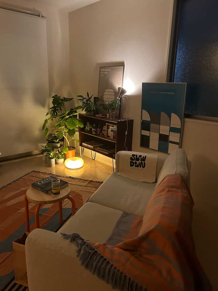 Natural color and wood tone living room featuring a cream sofa, patterned rug, and clustered plants creating cozy atmosphere
