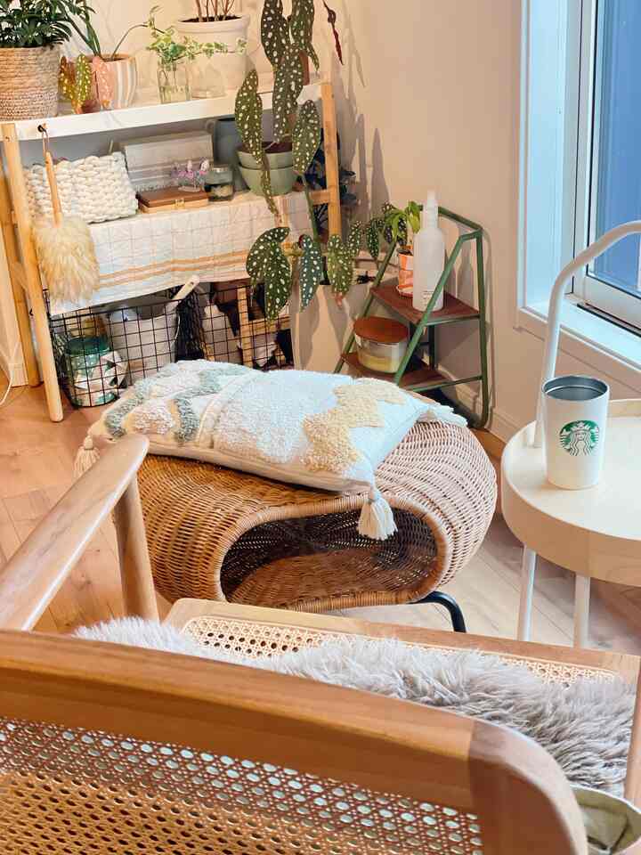 ナチュラルなブラウンとホワイトの色調のリビング、ラタンオットマンとクッション、棚や植物が配置された雰囲気のあるインテリア