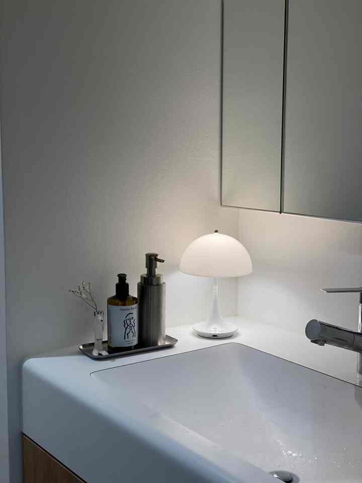 白を基調としたバスルームの洗面スペース、テーブルランプと清潔感あるディスペンサーが配置されたモダンなインテリア