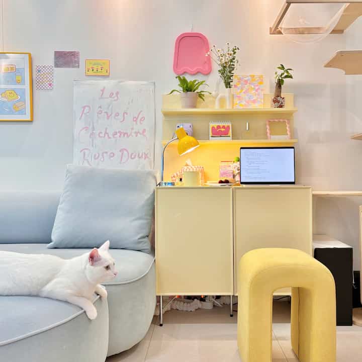 黄色とパステルトーンが調和するリビング、ベージュのキャビネットと黄色のスツール、ファブリックソファ、白猫がいる居心地の良い空間