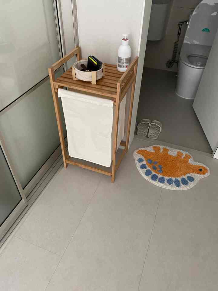 ナチュラルカラーの浴室前空間、スツールとスライディング洗濯かごが配置されたシンプルで実用的なインテリア