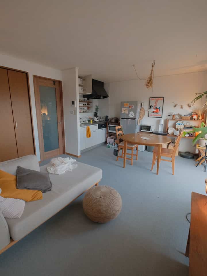 Natural wood-toned compact living room and kitchen featuring a round dining table and sofa with a cozy atmosphere