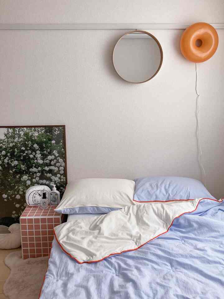 白と青のトーンが特徴の一人暮らし用寝室、ミッドセンチュリーモダンスタイルのタイルテーブルと丸い壁掛け鏡が配置された落ち着いた印象の空間