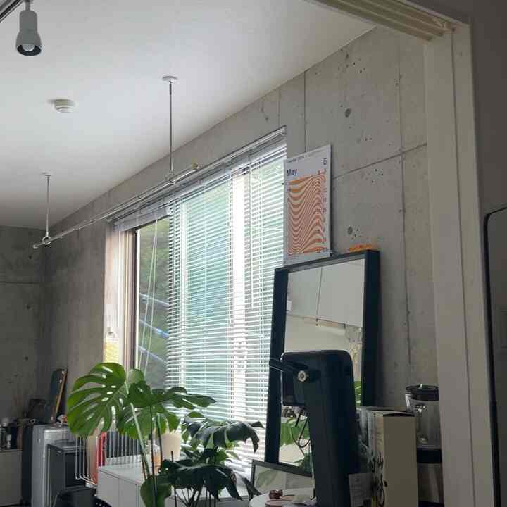 白とコンクリート調のモダンなキッチン空間、大きな窓のブラインドとテーブル上の植物が配置された雰囲気のあるインテリア